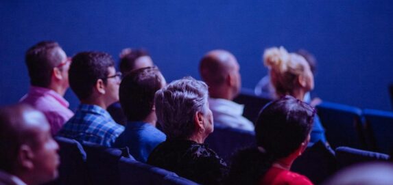 An attentive group of adults seated at an indoor conference, focusing on a presentation.